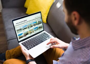 Rear view of a man looking for new houses on sale online. Young man using a real estate website on the laptop