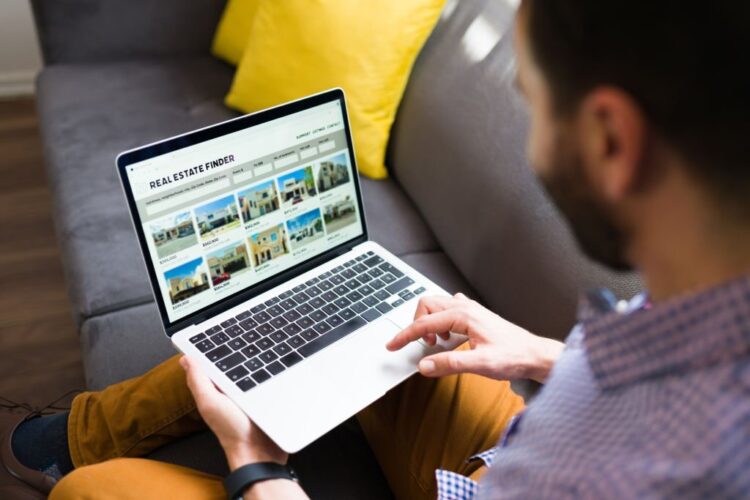 Rear view of a man looking for new houses on sale online. Young man using a real estate website on the laptop