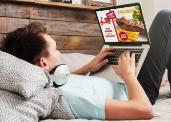 Man ordering take away food by internet with a laptop while lying at home.